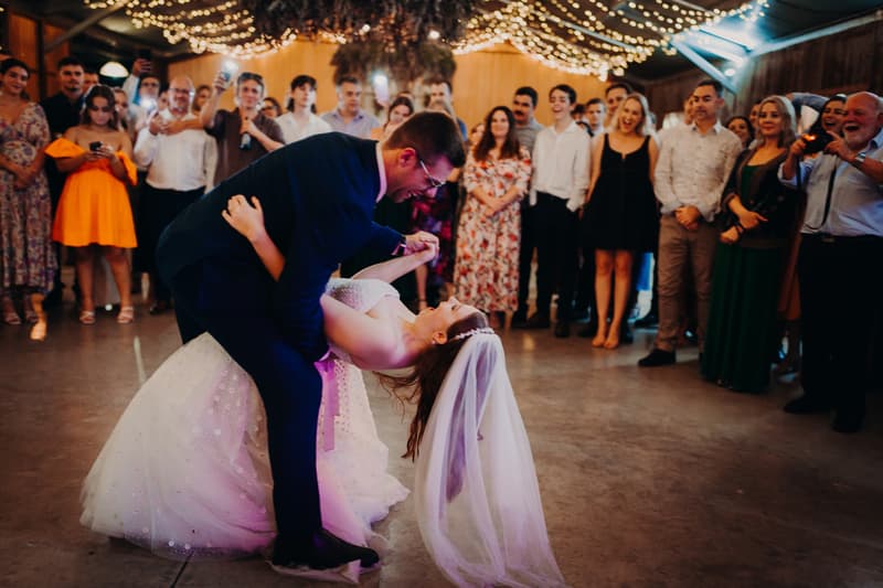 The bride Lilly and groom Connor share a dance on the floor at Yabbaloumba Retreat — The Shed while guests watch and take photos.