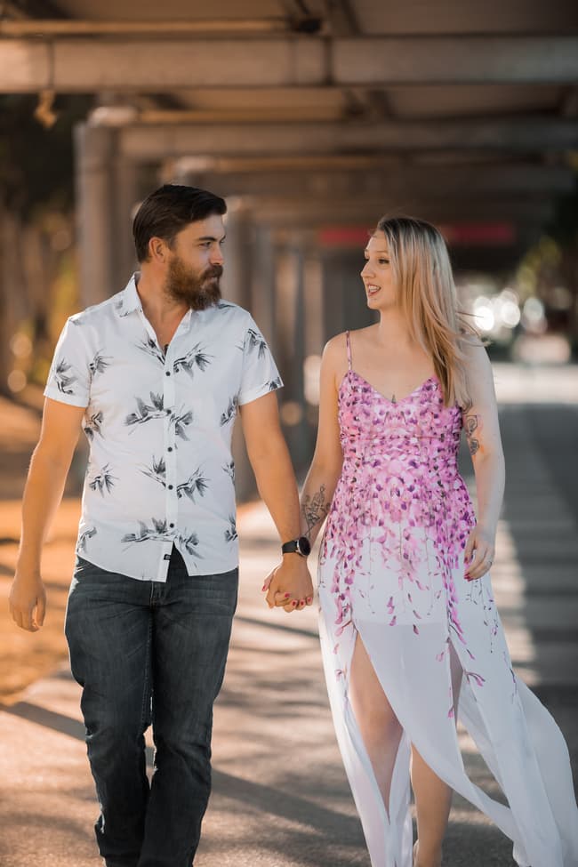 The couple walking hand in hand under a covered walkway at Brisbane Powerhouse, with soft sunlight illuminating them.