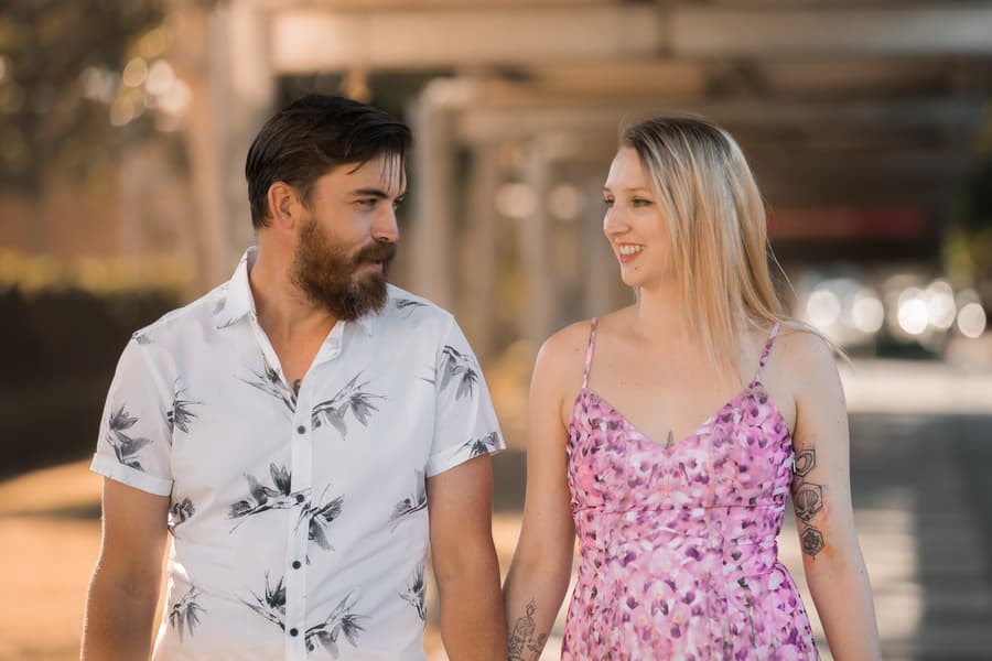 The couple walking side by side, looking at each other with smiles, under the covered walkway at Brisbane Powerhouse.