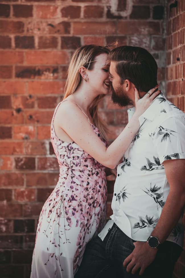 The couple standing close, gazing into each other's eyes, with a brick wall in the background at Brisbane Powerhouse.