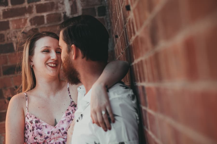 The couple embracing against a brick wall, sharing a tender moment at Brisbane Powerhouse.