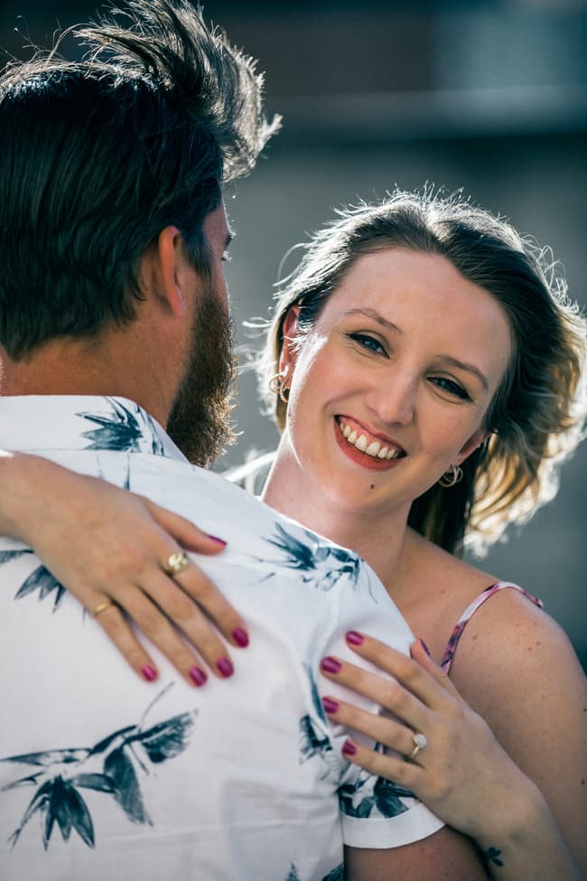 The couple standing outdoors, with the wind gently blowing their hair, smiling at each other.