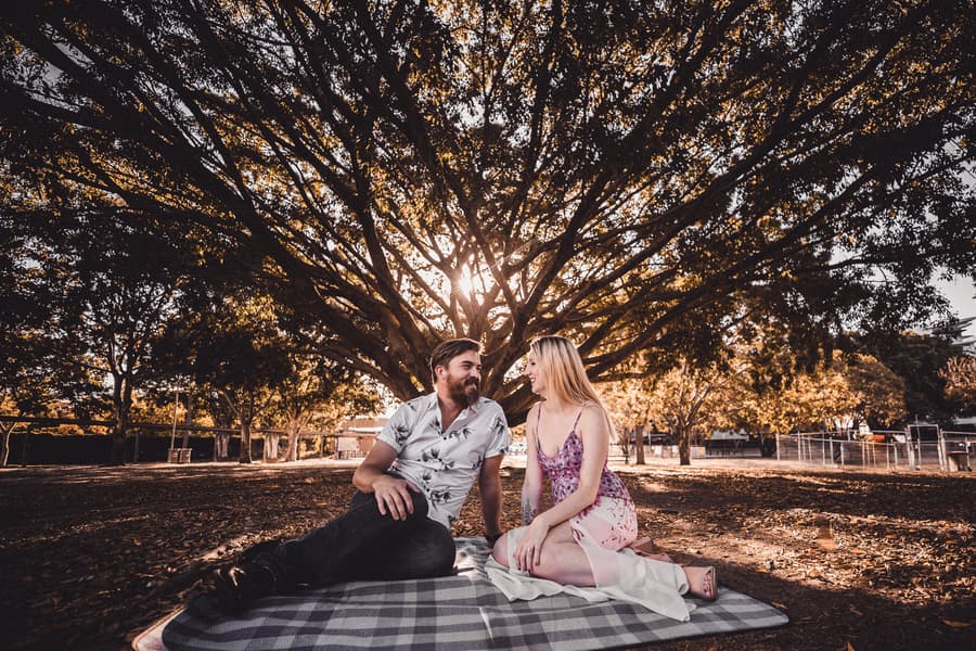 Close-up of the couple embracing, with one smiling warmly at the camera, outdoors at Brisbane Powerhouse.