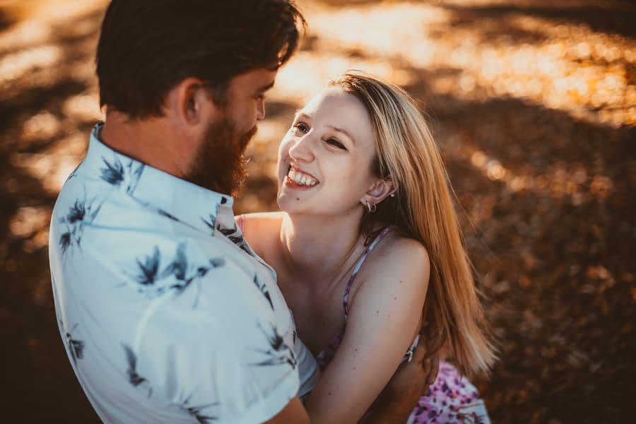 The couple standing close, gazing into each other's eyes with smiles, surrounded by fallen leaves at Brisbane Powerhouse.
