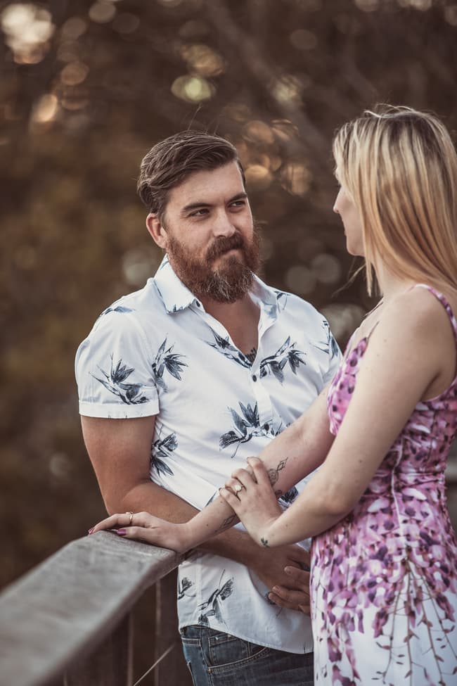 The couple standing on a balcony at Brisbane Powerhouse, holding hands and looking at each other with soft smiles.