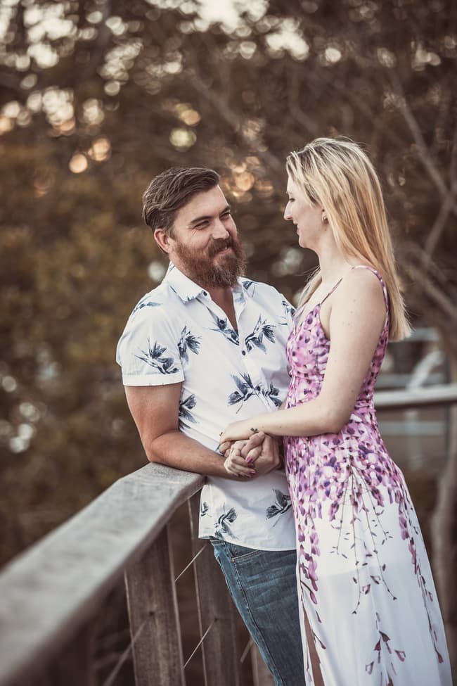 The couple standing on a balcony at Brisbane Powerhouse, holding hands and smiling warmly at each other.