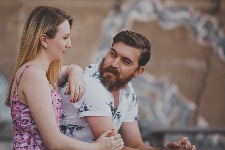 The couple sitting closely on a ledge at Brisbane Powerhouse, with one resting their arm on the other's shoulder, looking into each other's eyes.