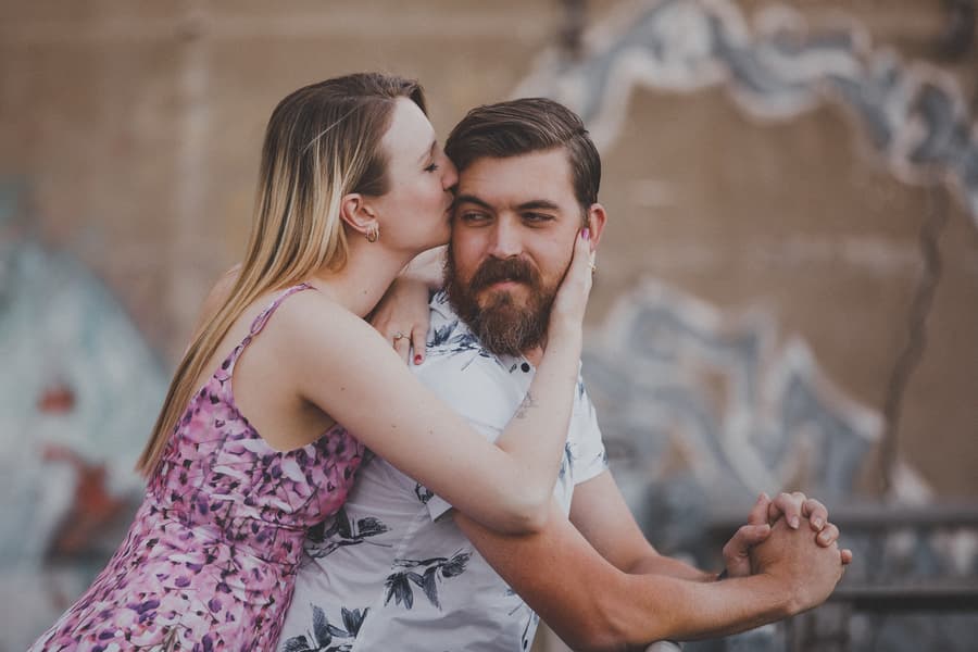 The couple at Brisbane Powerhouse, with one kissing the other's cheek, against a graffiti wall.
