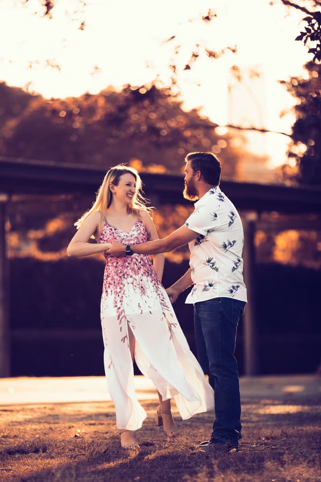 The couple dancing playfully on a sunlit lawn, surrounded by trees at Brisbane Powerhouse.