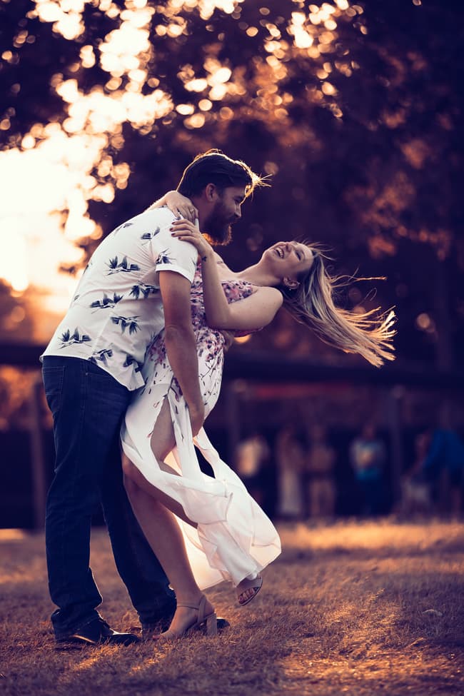 The couple laughing as one dips the other playfully, with trees in the background at Brisbane Powerhouse.