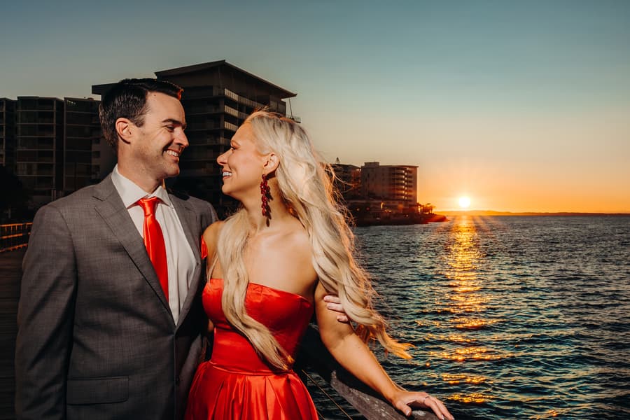 The couple gazes at each other lovingly, standing by the ocean at sunset.
