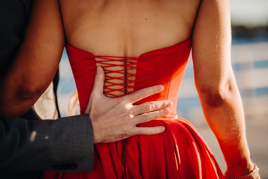 Close-up of a hand resting on the back of a red dress, showing the lacing detail.