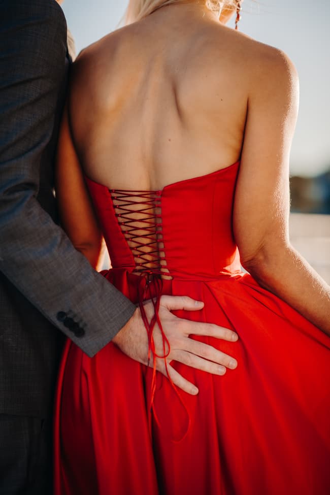 Close-up of a hand gently placed on the back of a red dress, highlighting the fabric's texture.