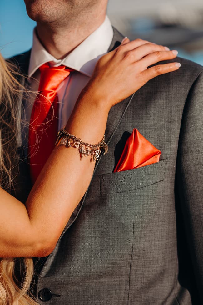 Close-up of a couple at Woody Point Jetty, with one wearing a gray suit and red tie, and the other resting a hand on their shoulder.