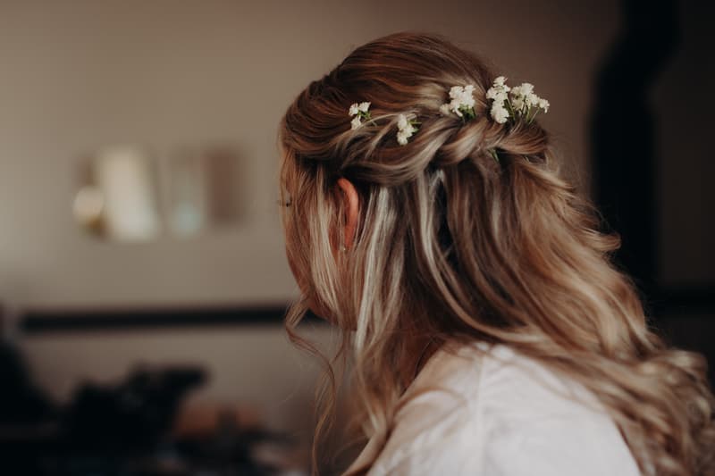 Close-up rear view of the bride Annie's styled hair with small white flowers woven into a braid, indoors.