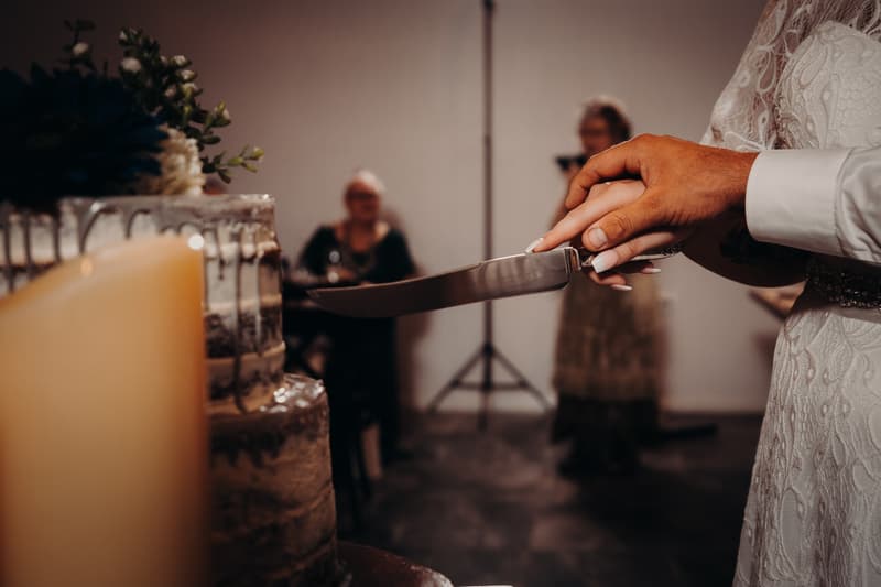 The bride Annie and groom Trent hold a knife together to cut the wedding cake at Ocean View Estates reception.