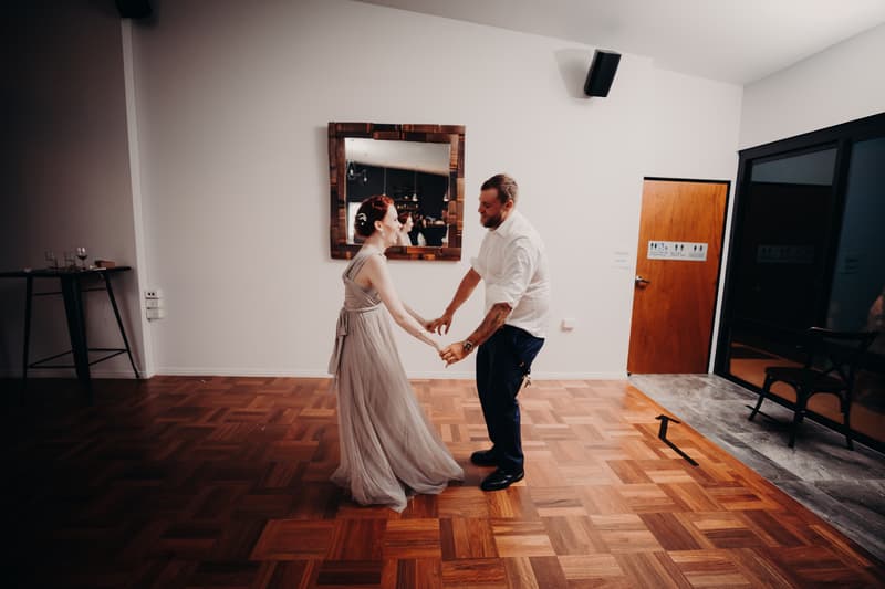 The bride Annie and groom Trent hold hands and dance on the wooden floor at Ocean View Estates reception stage.