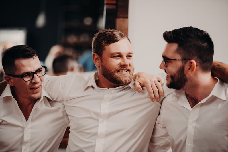 Three men in white shirts with arms around each other smiling and talking at Ocean View Estates reception stage.