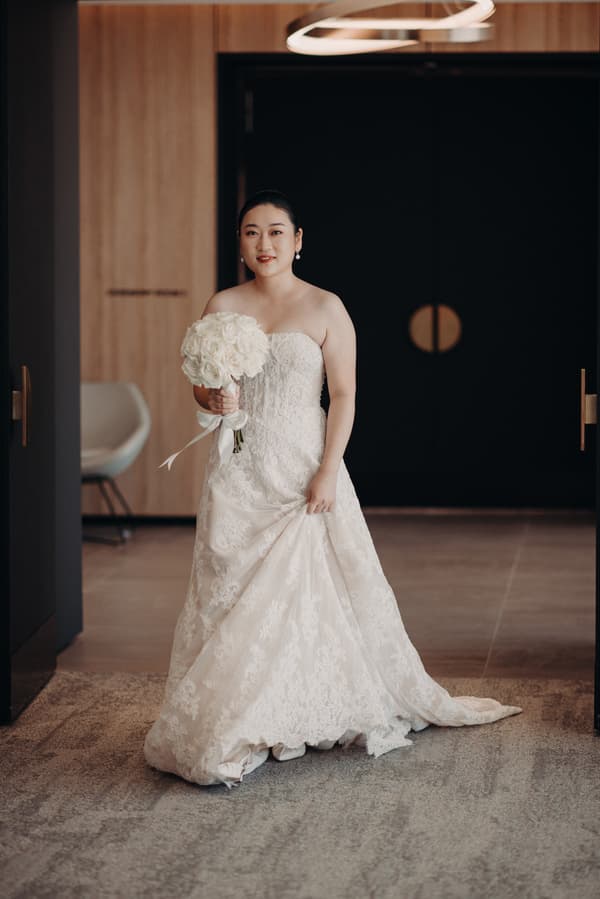 The bride Aria stands alone holding a bouquet of white roses inside the ceremony room at Brisbane Registry.