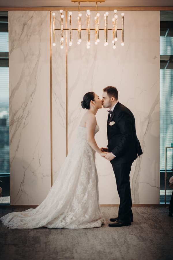 The bride Aria and the groom Antony share a kiss while holding hands in the ceremony room at Brisbane registry.