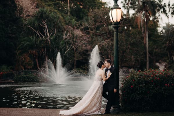 The bride Aria and the groom Antony share a close moment by a lamppost near a fountain in the City Botanic Gardens.