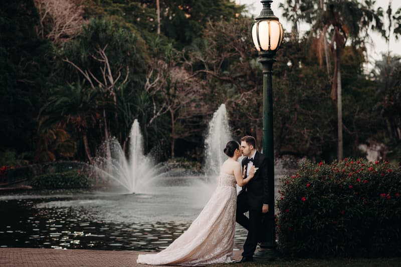The bride Aria and the groom Antony share a close moment by a lamppost near a fountain in the City Botanic Gardens.