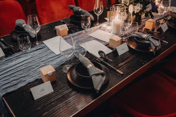 Table setting at Donna Chang with black plates, gray napkins, wine glasses, menus, small gift boxes, and name cards for guests including Ella and Charlotte.