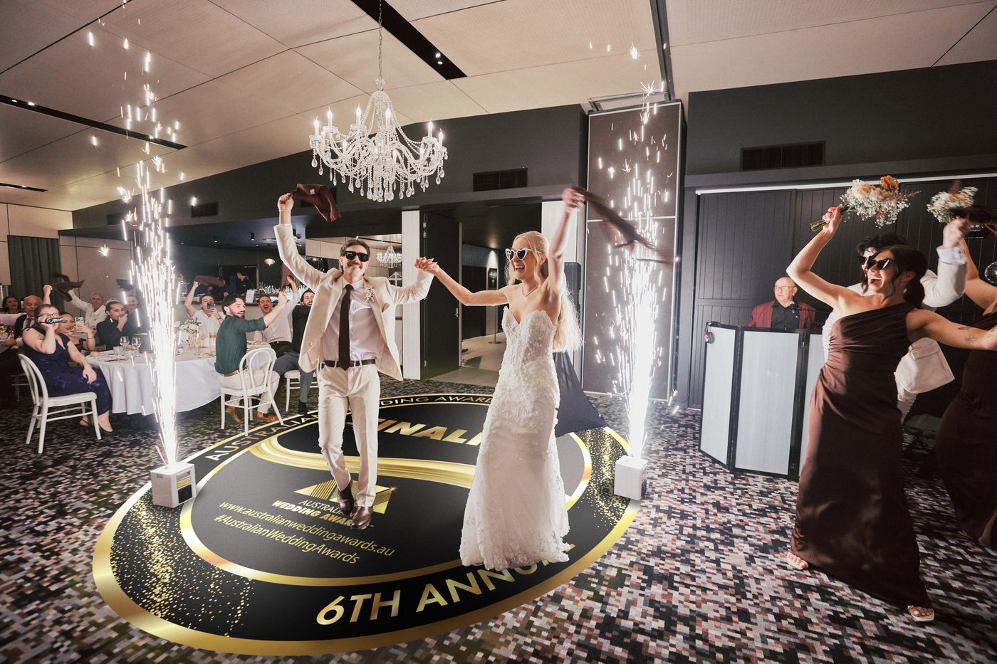 Morgan and Joel dancing into their Sandstone Point Hotel reception between sparkler fountains, across a floor decal of the 2026 Australian Wedding Awards Finalist roundel