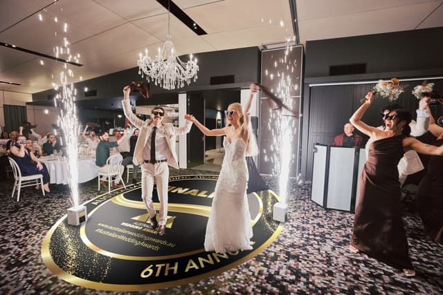 Morgan and Joel dancing into their Sandstone Point Hotel reception between sparkler fountains, across a floor decal of the 2026 Australian Wedding Awards Finalist roundel