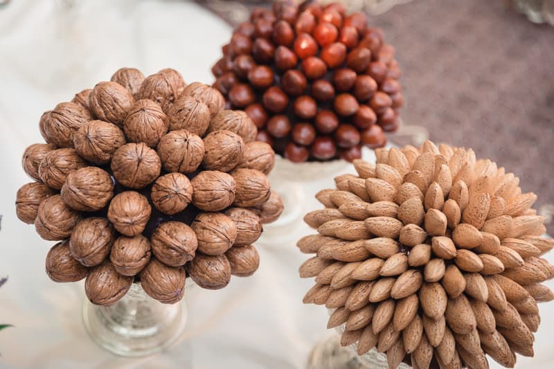 Close-up of three decorative arrangements made from walnuts, almonds, and hazelnuts placed on glass stands on a table.