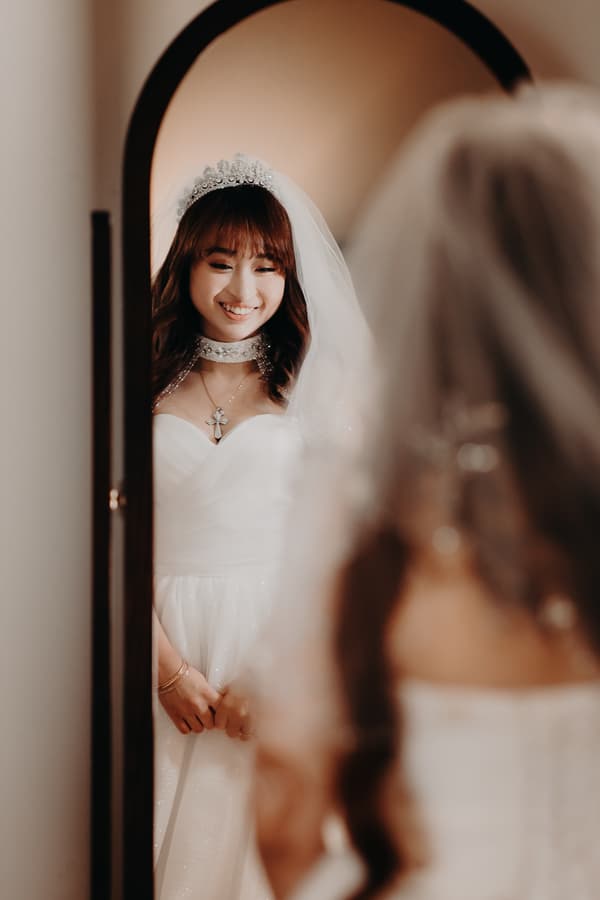 The bride Henny smiles while looking at herself in a mirror, wearing a white wedding gown, veil, and tiara at Royal on the Park.