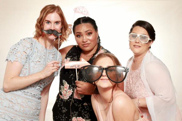 Four guests posing with props in a photo booth, wearing silly glasses and a crown.