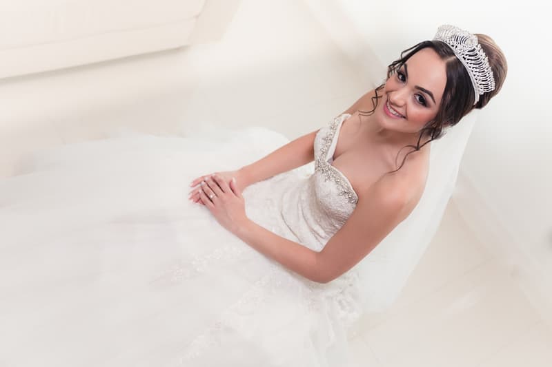 The bride Maryam sits on the floor in her wedding gown and tiara, smiling and looking up at the camera.