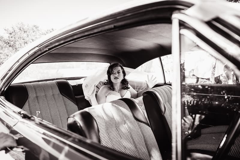 The bride Holly sits inside a vintage car at Kwila Lodge, visible through the open window.