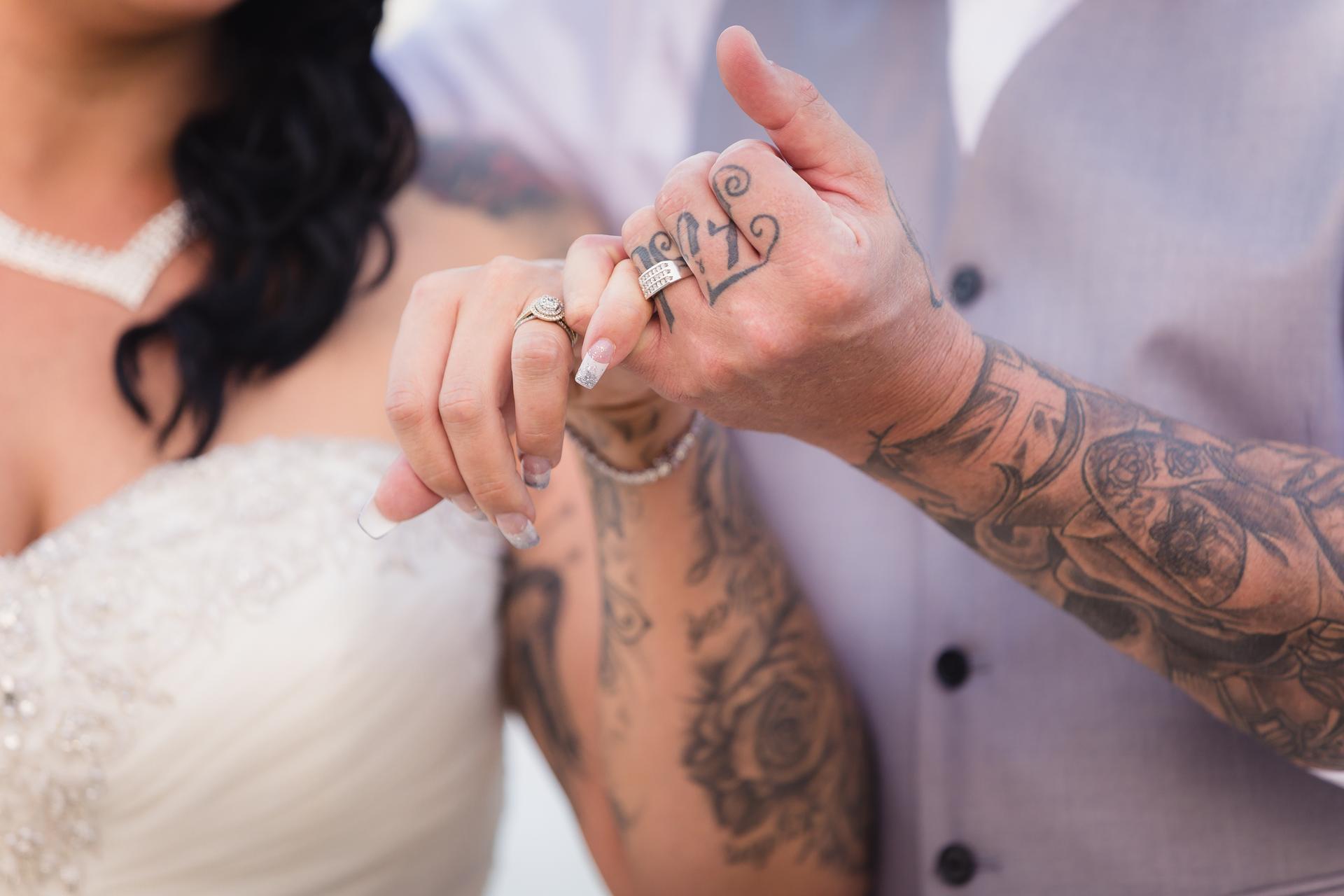 The bride and groom at Novotel Sunshine Coast Resort link pinky fingers, showing their wedding rings and tattoos on their arms.