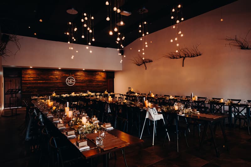 Reception tables set with candles, glassware, and floral centerpieces at Ocean View Estates, with hanging lights and wall decorations visible; no people present.