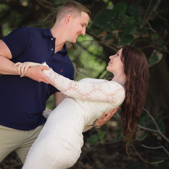 A couple dancing playfully under the trees. The man dips the woman, both smiling joyfully.