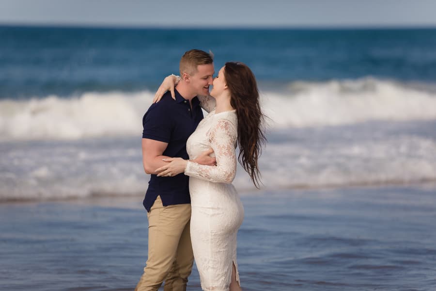 A couple standing in the shallow waves at The Spit, Gold Coast, embracing and smiling at each other.