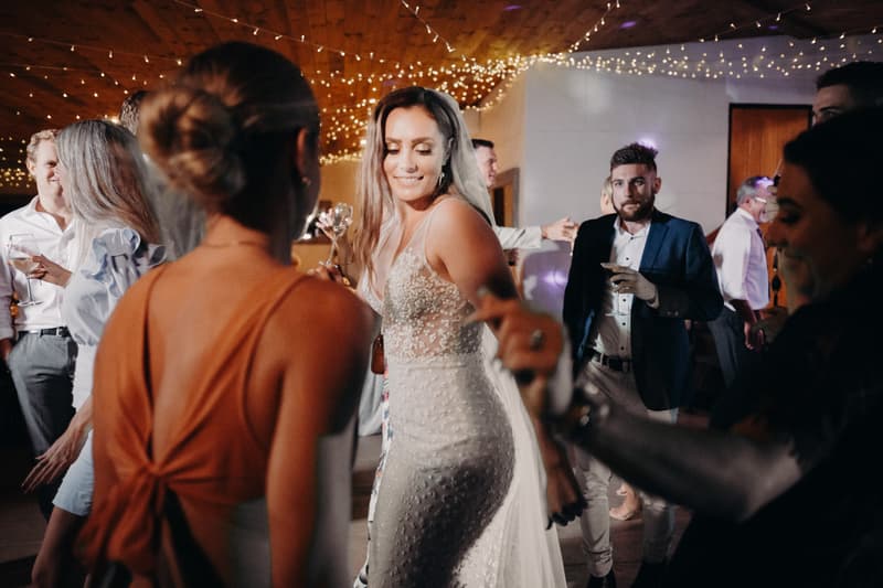 The bride Chelsea dances among guests at the Preston Peak Winery Functions Centre reception, with the groom Brent visible in the background holding a drink.