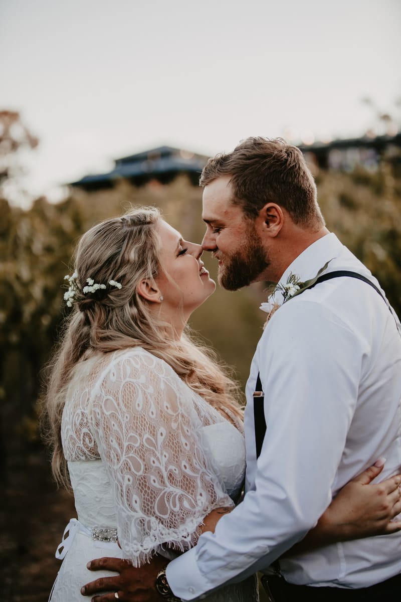 Annie and Trent embrace closely outdoors, with Annie wearing a lace wedding dress and floral hair accents, and Trent in a white shirt with suspenders and boutonniere. Elopement photography packages Brisbane by She Said Yes.