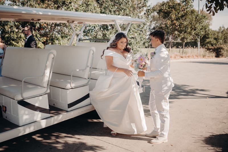 Bride Brooke in a white wedding gown and bride Tiffany in a white suit stand beside a white golf cart, with Brooke holding a bouquet of flowers. Elopement photography packages Queensland by She Said Yes.