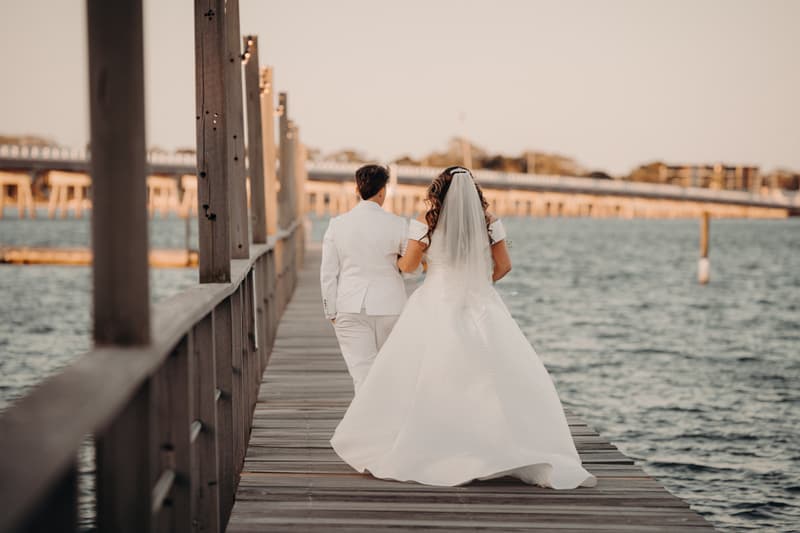 Brooke and Tiffany walk arm in arm along a wooden jetty over water at Sandstone Point Hotel.