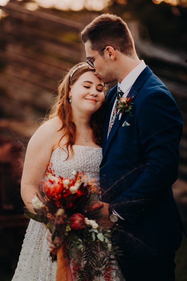 Lilly and Connor share a tender moment during their couple portraits at Yabbaloumba Retreat, with Connor kissing Lilly's forehead as she holds a bouquet of flowers.