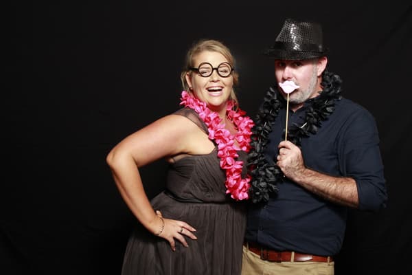 Two guests posing with props and leis in a photo booth.