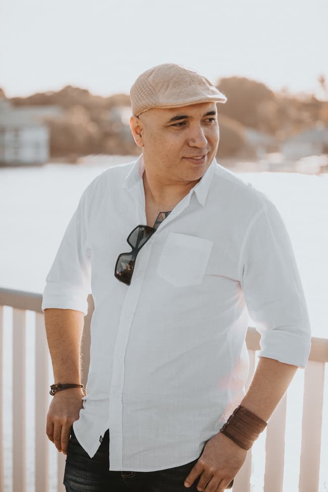 A person in a white shirt and cap stands by a railing with water in the background at Novotel Twin Waters.
