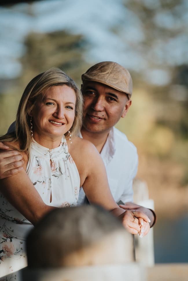 The couple sits closely on a bench, with one person leaning against the other, smiling warmly.