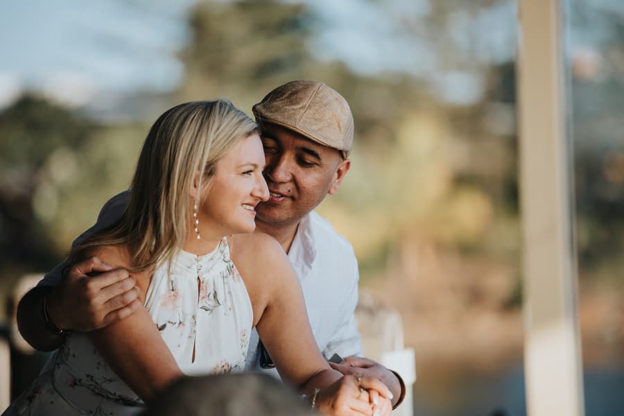 The couple shares a close moment, smiling at each other, with a blurred natural background.