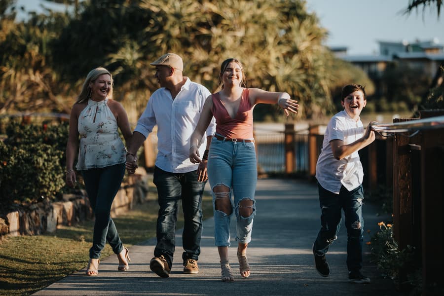 A family of four walks together, laughing and enjoying each other's company on a sunny day.
