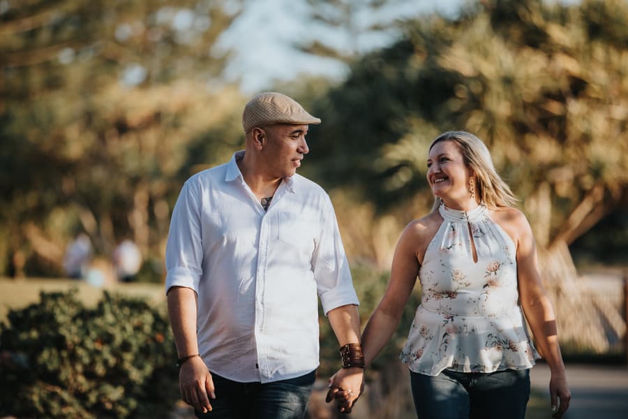 The couple walking hand in hand at Novotel Twin Waters, surrounded by greenery and soft sunlight.