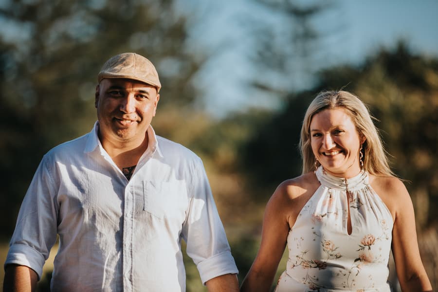 Close-up of the couple smiling warmly at the camera, with trees softly blurred in the background.